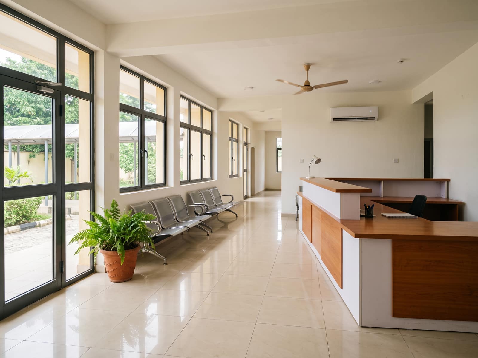 The entrance hall of a hospital, with a reception counter and rows of chairs in morning light